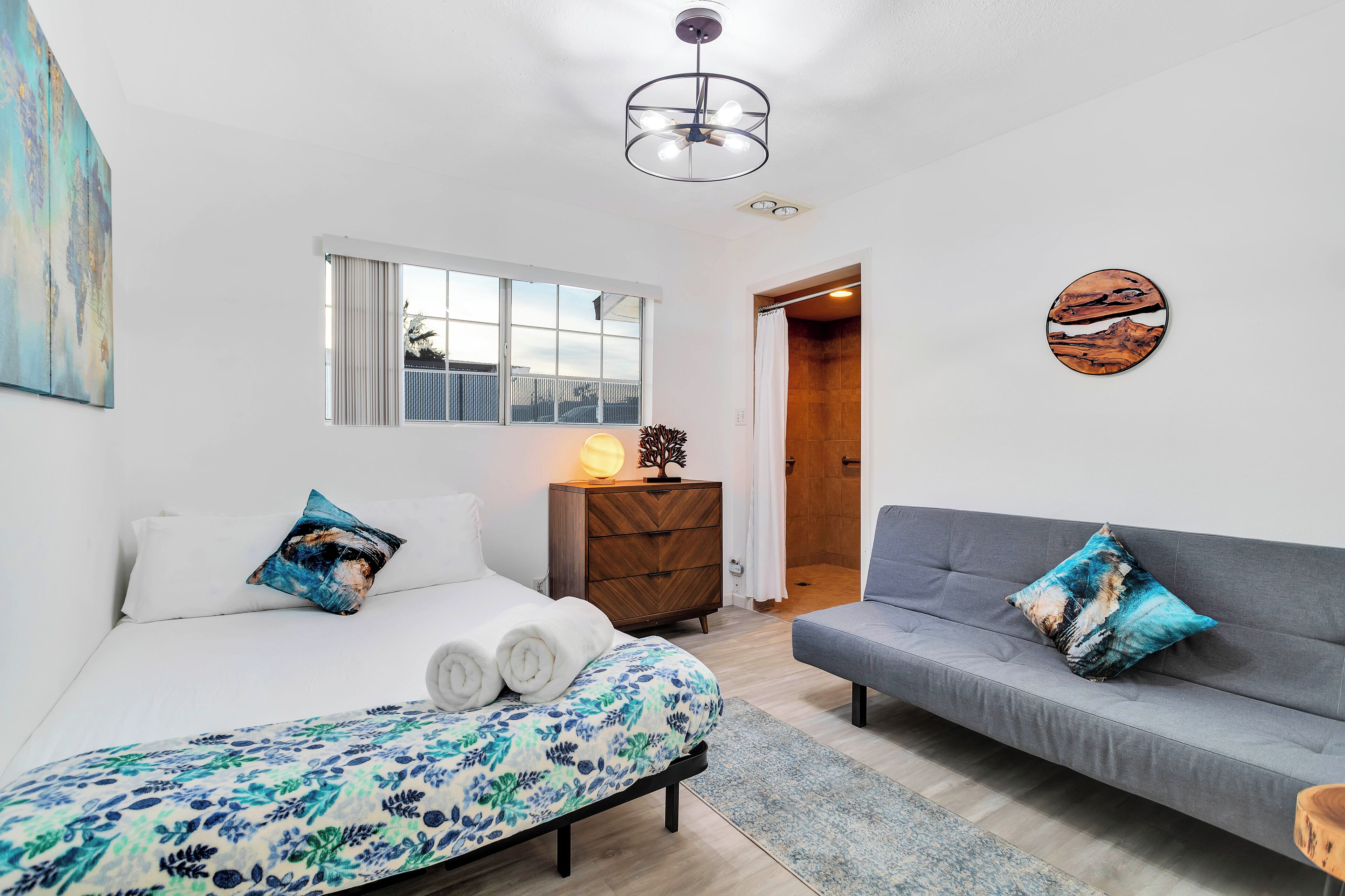 A modern bedroom with a bed, a sofa, a dresser, and a window.