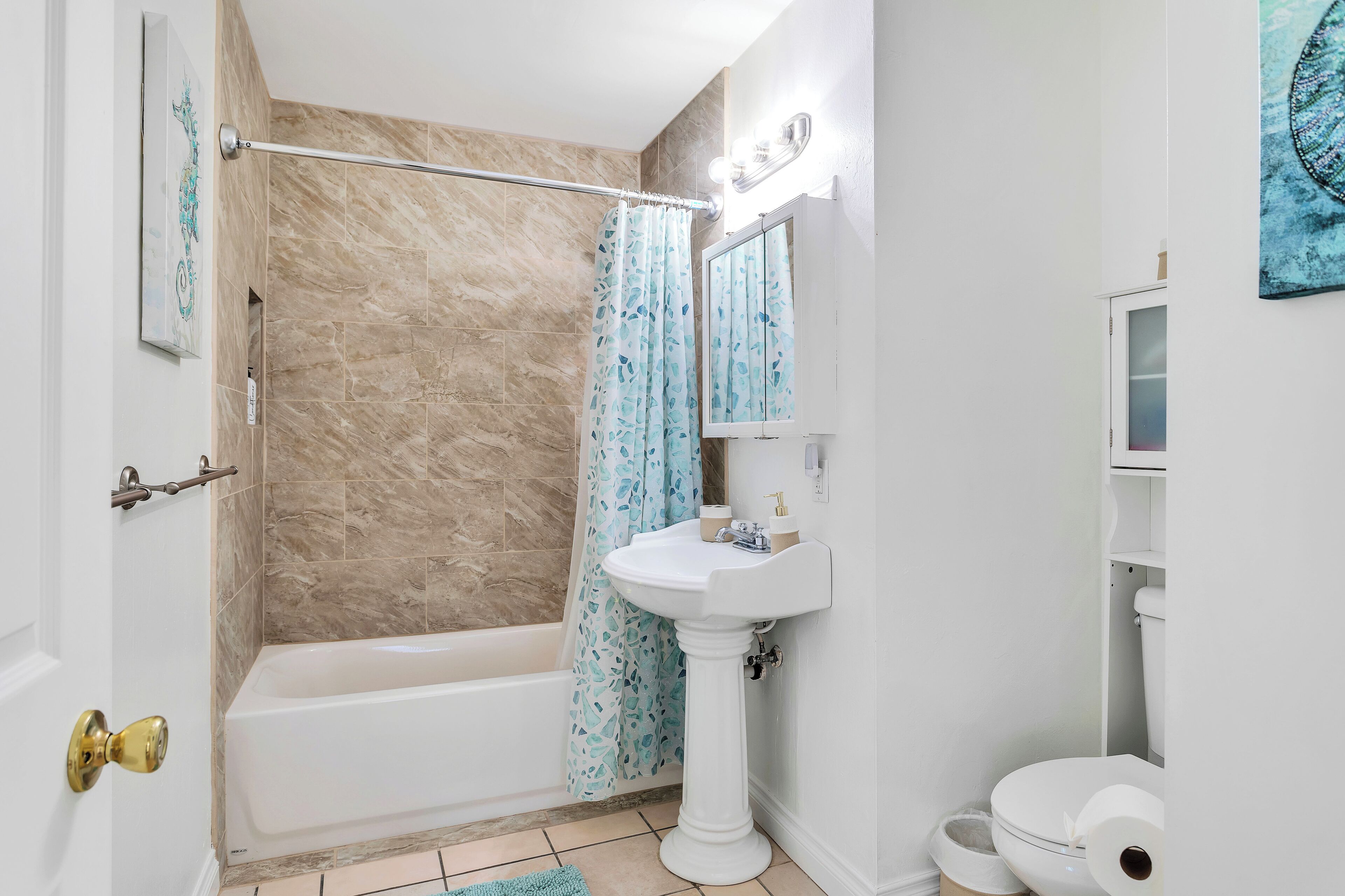 A bathroom with a bathtub, a pedestal sink, and a toilet.