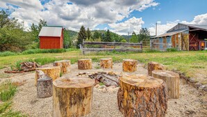 A rustic outdoor setting with wooden stumps arranged in a circle, a red barn, and a wooden fence in the background. - Historic 'mcbride House' in Garden Valley Mtns! (Garden Valley)