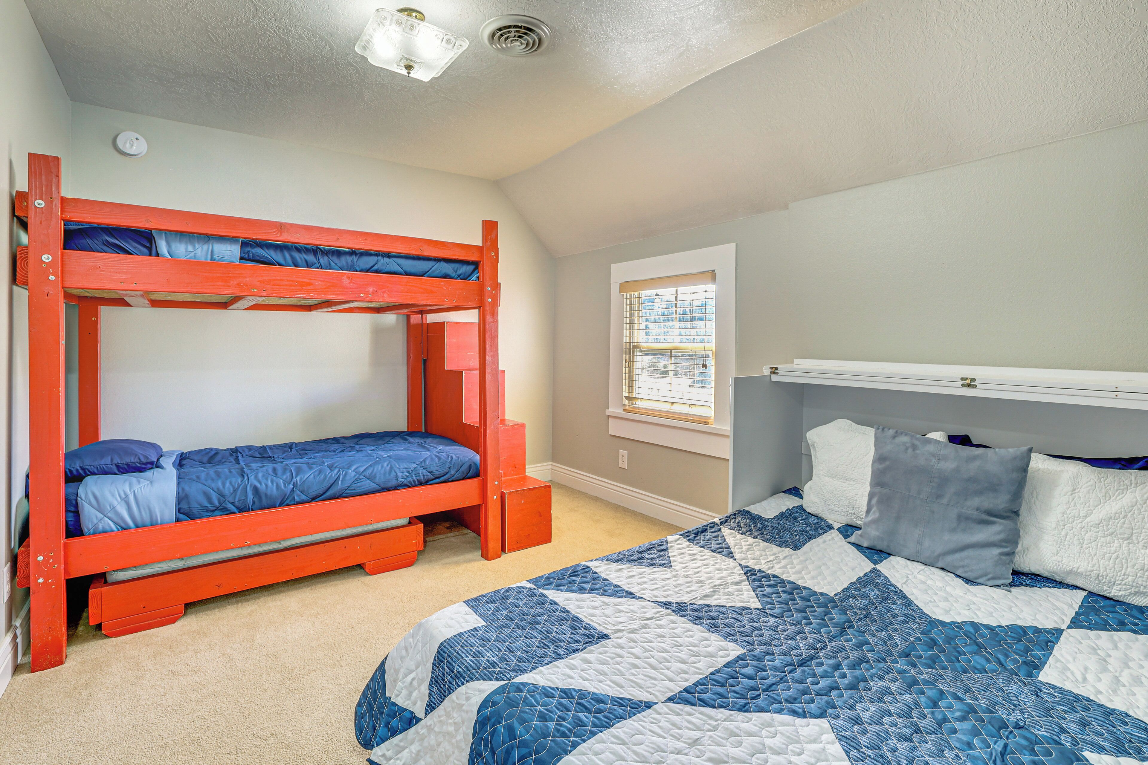 A bedroom with a bunk bed, a single bed with a quilt, a window with blinds, and a ceiling light.