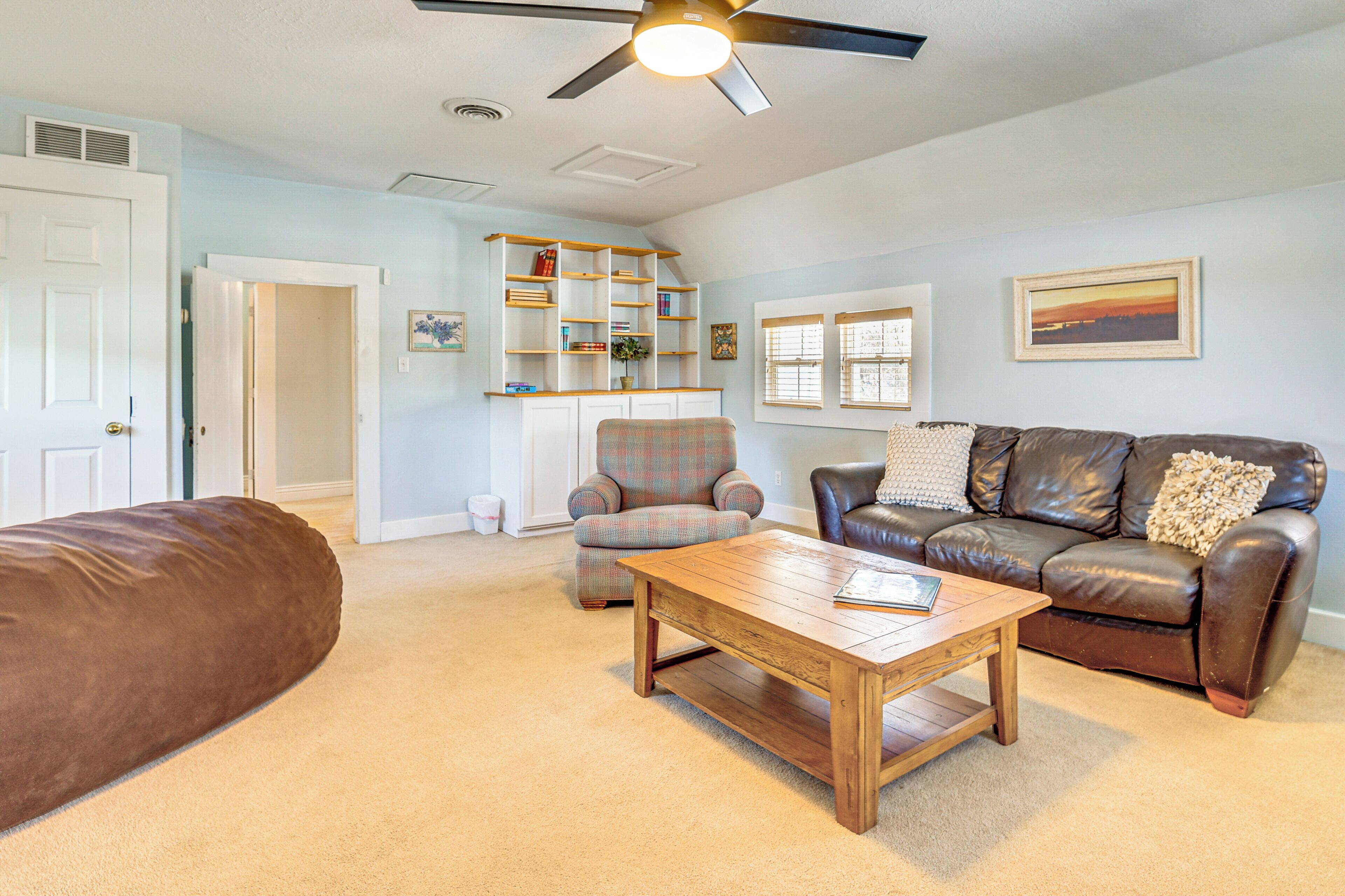 A living room with a brown leather sofa, a plaid armchair, a wooden coffee table, and a brown leather couch.