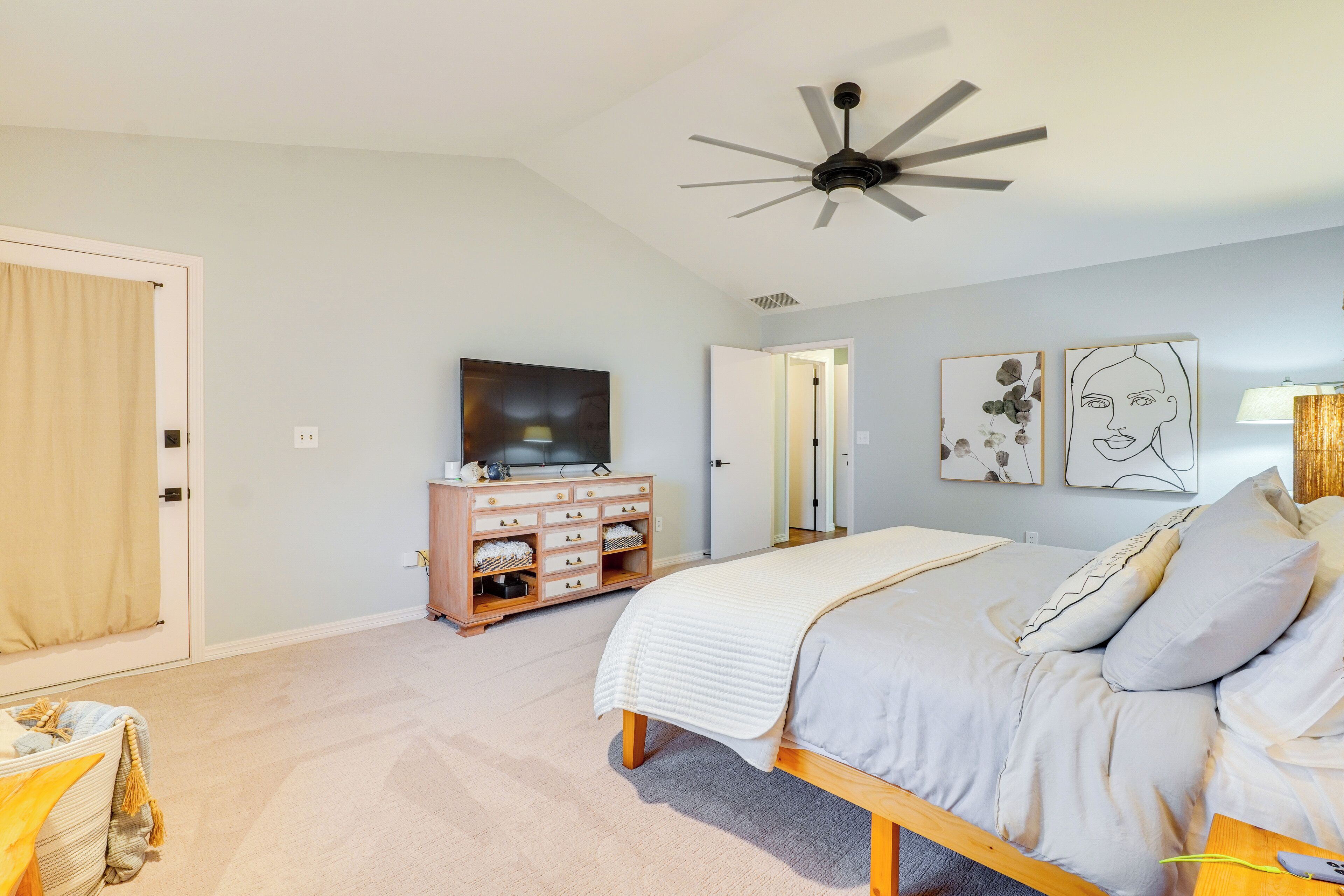 Une chambre à coucher avec un lit, un ventilateur de plafond, une commode et des œuvres d’art accrochées au mur.