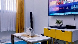 A modern living room with a flat-screen TV mounted on the wall, a small table with a decorative item, and a yellow and white cabinet. - Standard Gardens Milimani Kisumu (Kisumu)