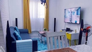 A modern living room with a dining area, featuring a sofa, a coffee table, a TV, and a fan. - Standard Gardens Milimani Kisumu (Kisumu)
