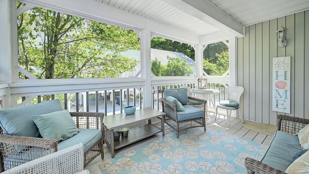 A covered porch with wicker furniture, a table, and a view of trees. - Charming 3 Bedroom Cottage in Bahama Beach Cottages! Dog Friendly, WIFI, Beach Town! (Bethany Beach)