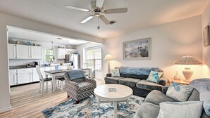 A modern living room with a sofa, armchair, and coffee table. There is a kitchen area with white cabinets and a dining table. A ceiling fan is visible above the living room. - Charming 3 Bedroom Cottage in Bahama Beach Cottages! Dog Friendly, WIFI, Beach Town! (Bethany Beach)