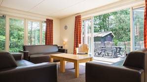 A cozy room with a sofa, chairs, a table, and large windows offering a view of the outdoors. - Summio Parc De Berkenhorst (Kootwijk)