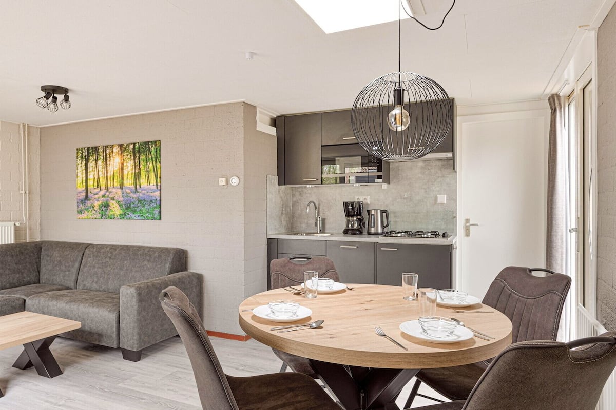 Un salon moderne avec un canapé gris, une table basse en bois et une table à manger pour quatre personnes.