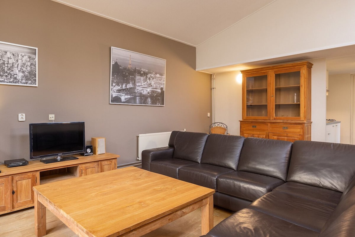 Un salon avec un canapé en cuir, une table basse en bois, un téléviseur et deux tableaux encadrés accrochés au mur.