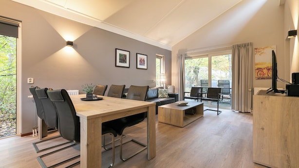 A modern living room with a wooden dining table, leather chairs, a sofa, and a TV on a wooden cabinet. - Summio Parc De Berkenhorst (Kootwijk)
