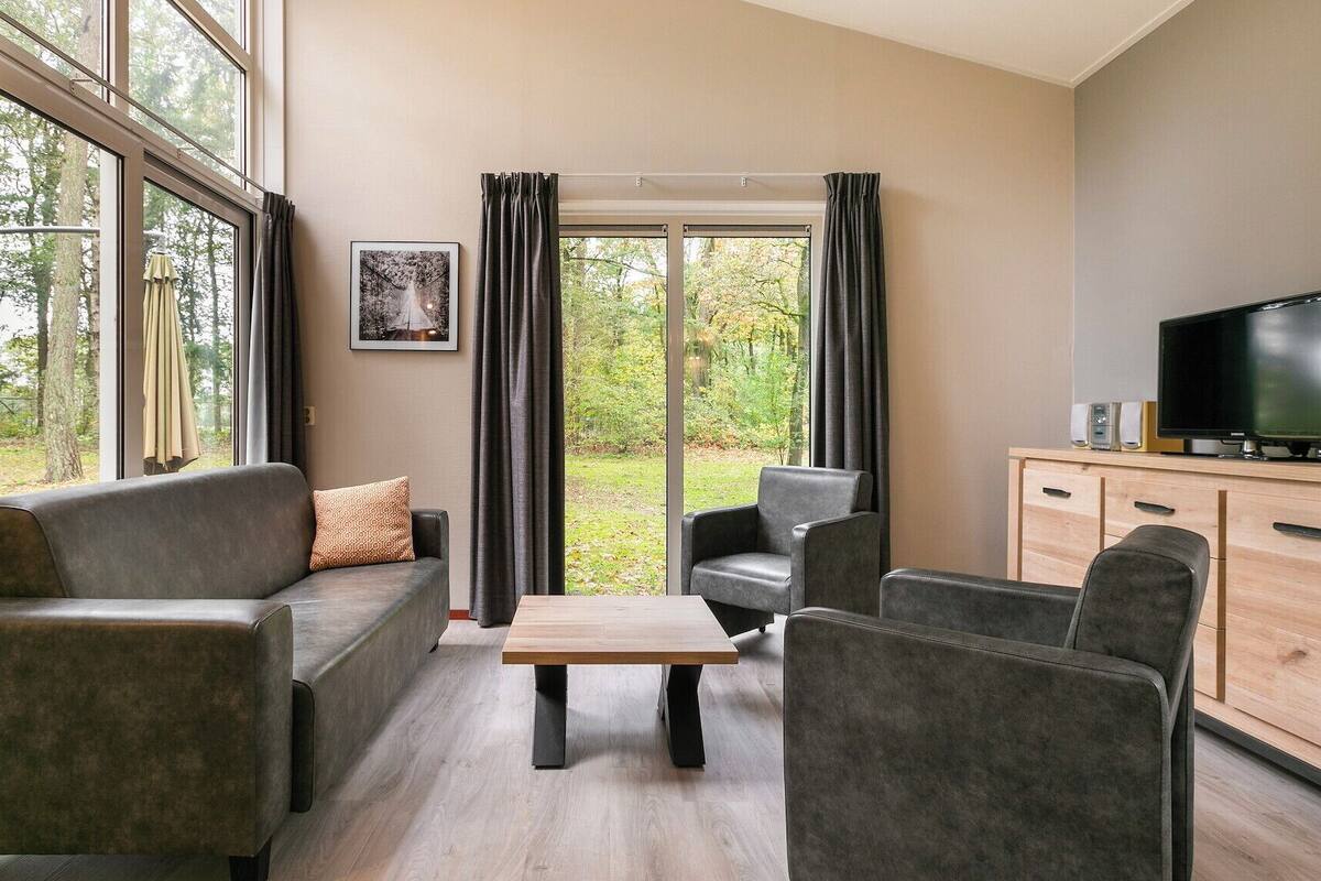 Un salon moderne avec un canapé, des fauteuils, une table basse et un téléviseur posé sur un meuble en bois.