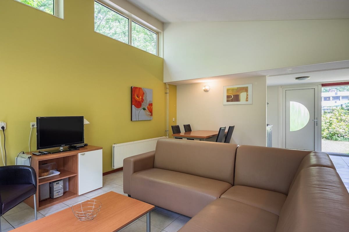Un salon moderne avec un canapé, un téléviseur et un coin repas équipé de chaises.