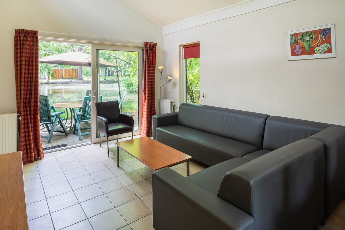 Un salon avec un canapé gris, une table basse en bois et une table à manger avec des chaises. Une porte-fenêtre coulissante donne accès à un espace extérieur équipé d’une table et de chaises.