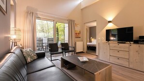 A modern living room with a sofa, chairs, a coffee table, a TV, and a dining area with a table and chairs. - Summio Parc De Berkenhorst (Kootwijk)
