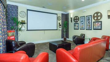 A home theater room with red and black leather seating, a large screen, and framed movie posters on the wall.