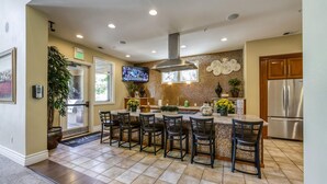 Una cocina moderna con una isla central, taburetes de bar, un refrigerador de acero inoxidable y un televisor montado en la pared.