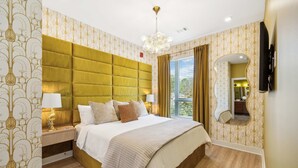 Habitació d'hotel amb un llit gran, un capçal de llit, una taula de nit amb làmpades, un mirall i una finestra amb cortines.