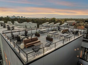 Une terrasse sur le toit avec des sièges extérieurs, des unités de climatisation et une vue sur la ville au coucher du soleil.