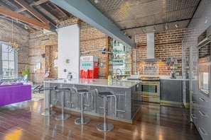 Enjoy cooking in this kitchen with a central island, oven, and stainless steel range hood, surrounded by exposed brick walls and a high ceiling.