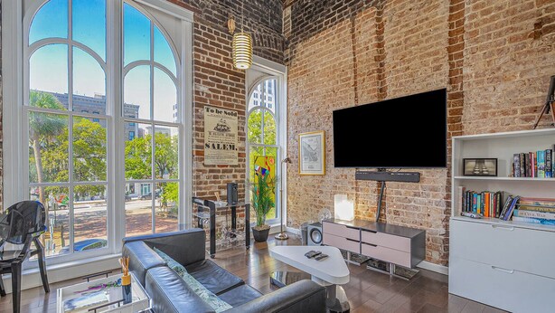 Een ruime woonkamer met een groot raam, een zwarte leren bank, een flatscreen televisie en een boekenkast.