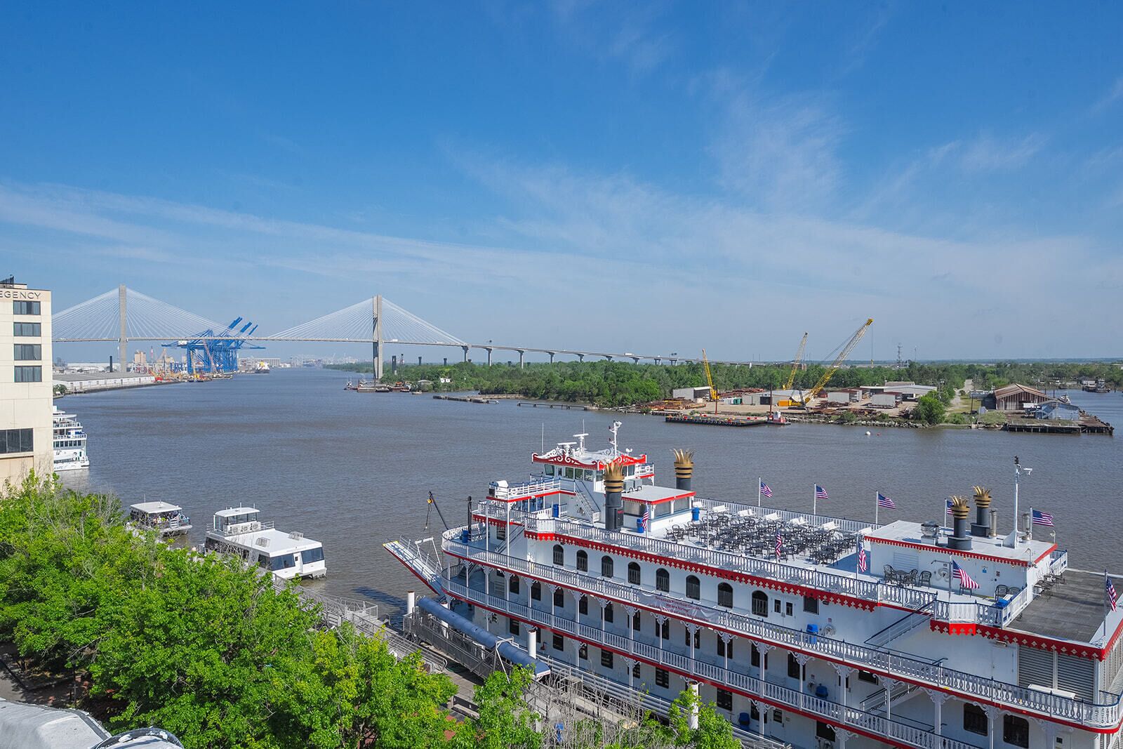 Ein großes Flusskreuzfahrtschiff liegt an einem Hafen, im Hintergrund ist eine Brücke zu sehen.