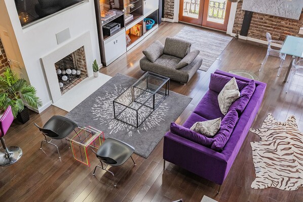 A modern living room with a fireplace, a purple sofa, a grey armchair, and a glass coffee table.