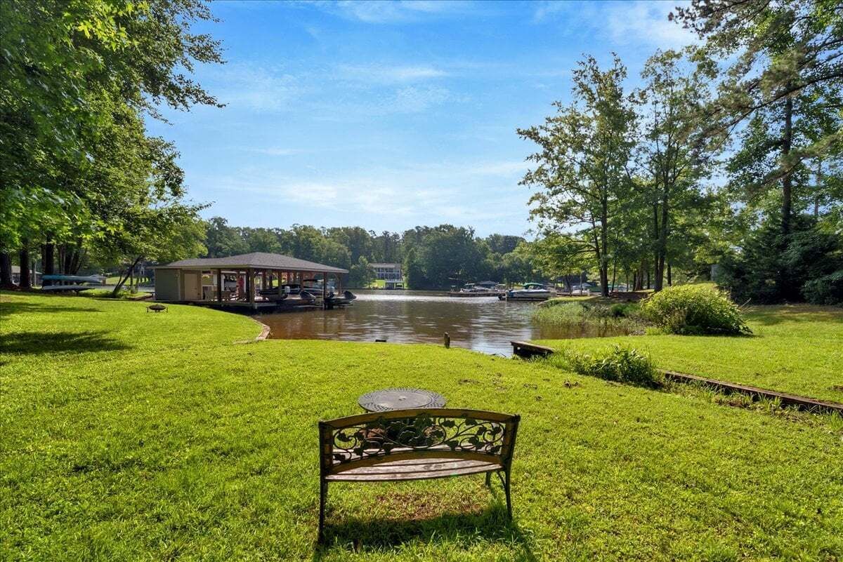 A grassy area with a bench, a gazebo, and a body of water with boats.