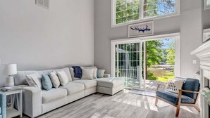 A living room with a sectional sofa, a side table, a lamp, a bench, and a view through large windows. - Tide & Timber | Community Swiming Pool | Pet-Friendly (Fee) (Littleton)