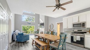 A modern kitchen with white cabinets, a stainless steel oven, and a microwave. There is a wooden dining table with chairs and a ceiling fan. - Tide & Timber | Community Swiming Pool | Pet-Friendly (Fee) (Littleton)