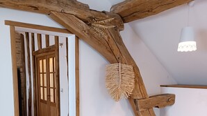 A room with exposed wooden beams, a woven rattan chair, and a wooden door. - Gîte Le Belvédère du Lac between lakes and castles of the Dukes of Burgundy (Civry-en-Montagne)