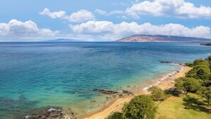 Un paysage côtier offrant une vue dégagée sur la mer, une plage de sable et un arrière-plan montagneux.