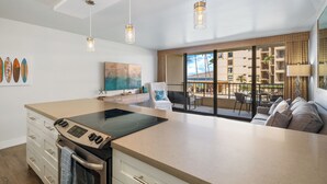 A modern kitchen with a large island, a dining area with a sofa, and a balcony with a view of the city. - Gorgeous Oceanfront Remodel I Sugar Beach 210 (Kihei)