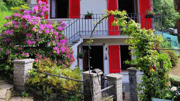 A two-story building with red shutters and a stone facade, featuring a balcony with potted plants and a sign reading "La Baita Alpina". - The mountain Cabin (scopa)