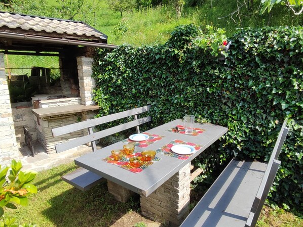 An outdoor patio with a stone barbecue and a table set with plates and bowls.