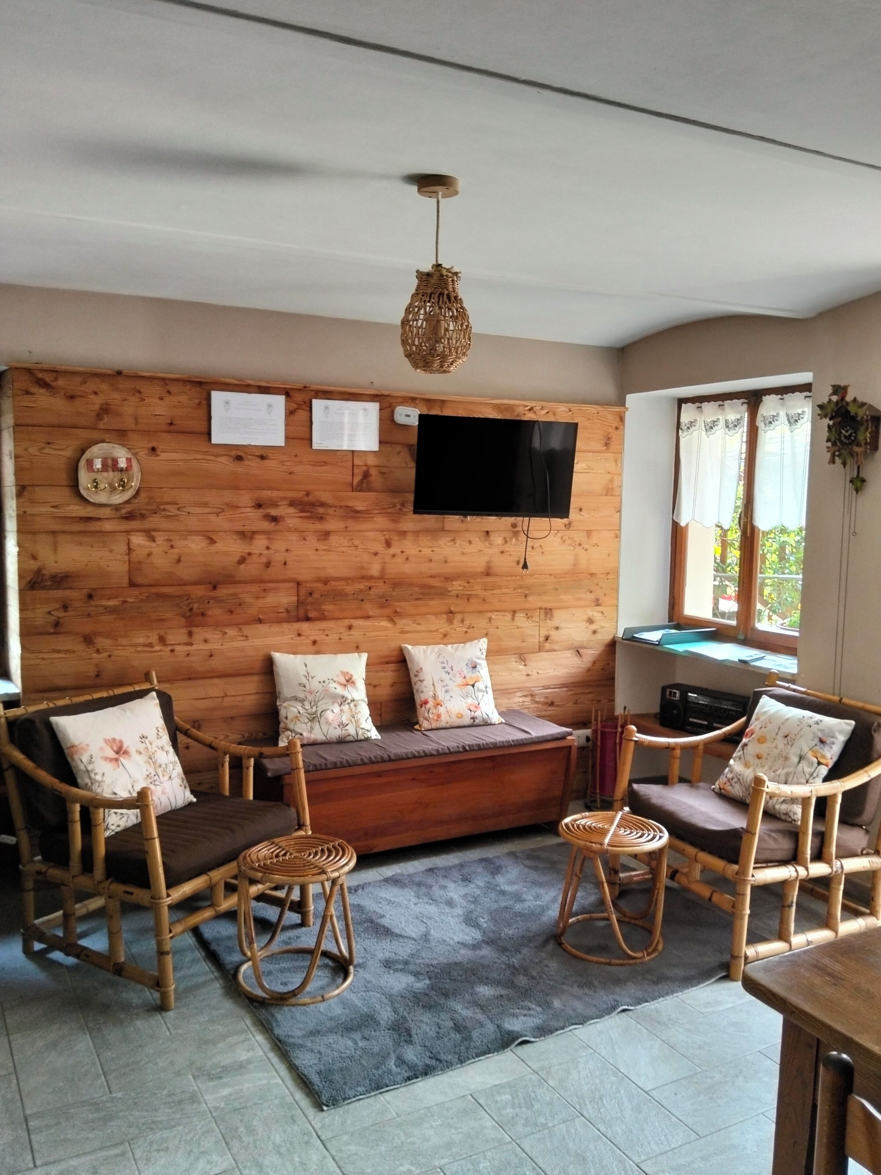 A cozy room with a wooden wall, a flat-screen TV, a sofa with floral cushions, and wicker chairs.