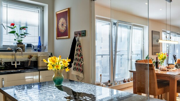 A modern kitchen with a marble countertop, a vase of flowers, and a dining area with a wooden table and chairs.
