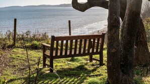 A wooden bench by a grassy area overlooking a body of water with a distant shoreline.