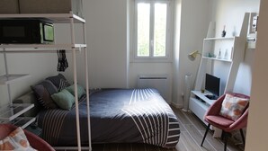 A compact bedroom with a bunk bed, a desk with a computer, a chair, and a window providing natural light. - Superbe Studio Neuf au Cœur des Carmes - Elegance & Comfort (Toulouse)