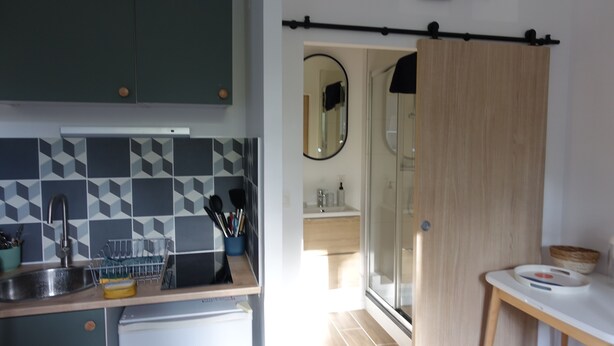 A modern kitchen with a geometric tile backsplash, a sink with utensils, and a wooden door leading to a bathroom. - Superbe Studio Neuf au Cœur des Carmes - Elegance & Comfort (Toulouse)