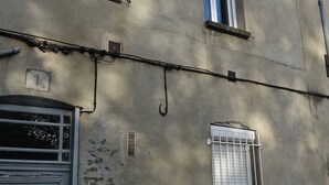 A building with multiple windows, some with shutters, and a door with a geometric design. There are visible cracks and patches on the walls, and a small plant is growing near the base of the building. - Superbe Studio Neuf au Cœur des Carmes - Elegance & Comfort (Toulouse)