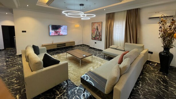 Un salon moderne avec un sol en marbre, un téléviseur à écran plat fixé au mur, un canapé, une table basse et un vase décoratif.