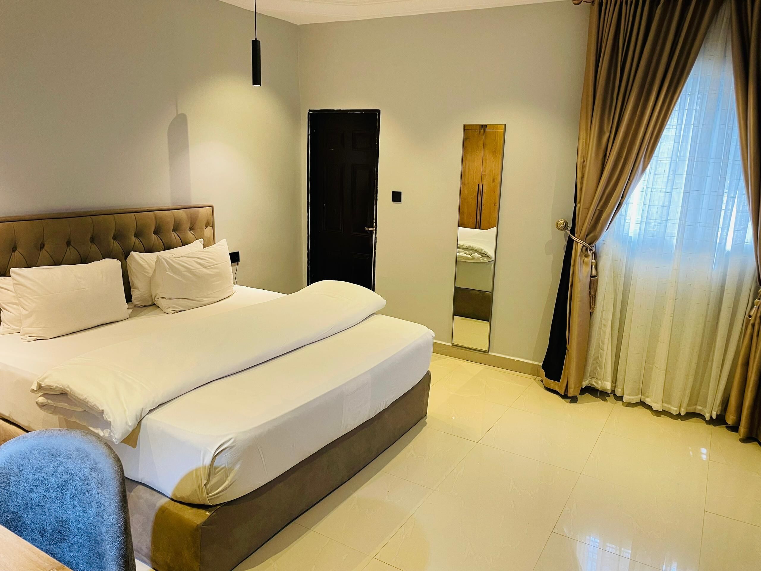 Una camera d'albergo con un letto grande, uno specchio, una porta e una finestra con tende.