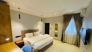 Une chambre d’hôtel moderne dotée d’un grand lit, d’un bureau, d’une chaise, d’un téléviseur à écran plat et d’une grande fenêtre avec des rideaux.