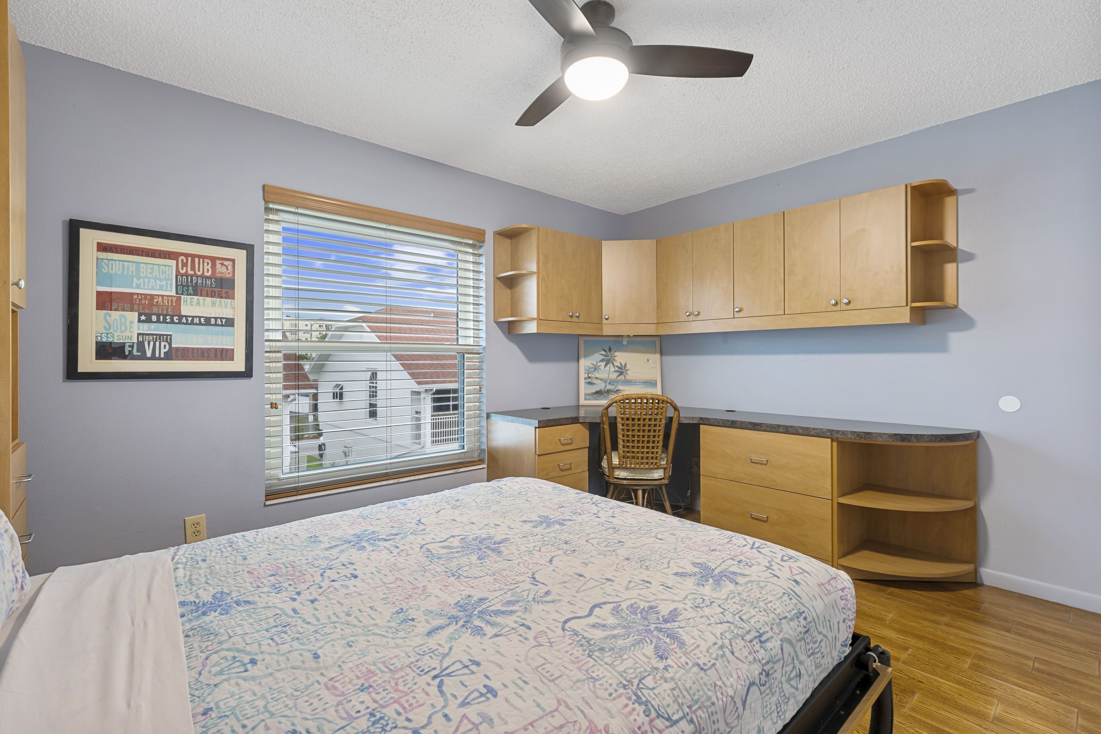 A bedroom with a bed, a desk, a chair, and a ceiling fan.