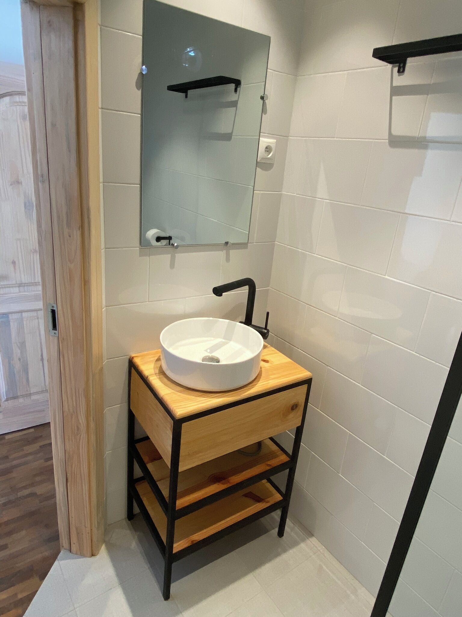 Un baño con lavamanos blanco, tocador de madera y espejo en la pared.