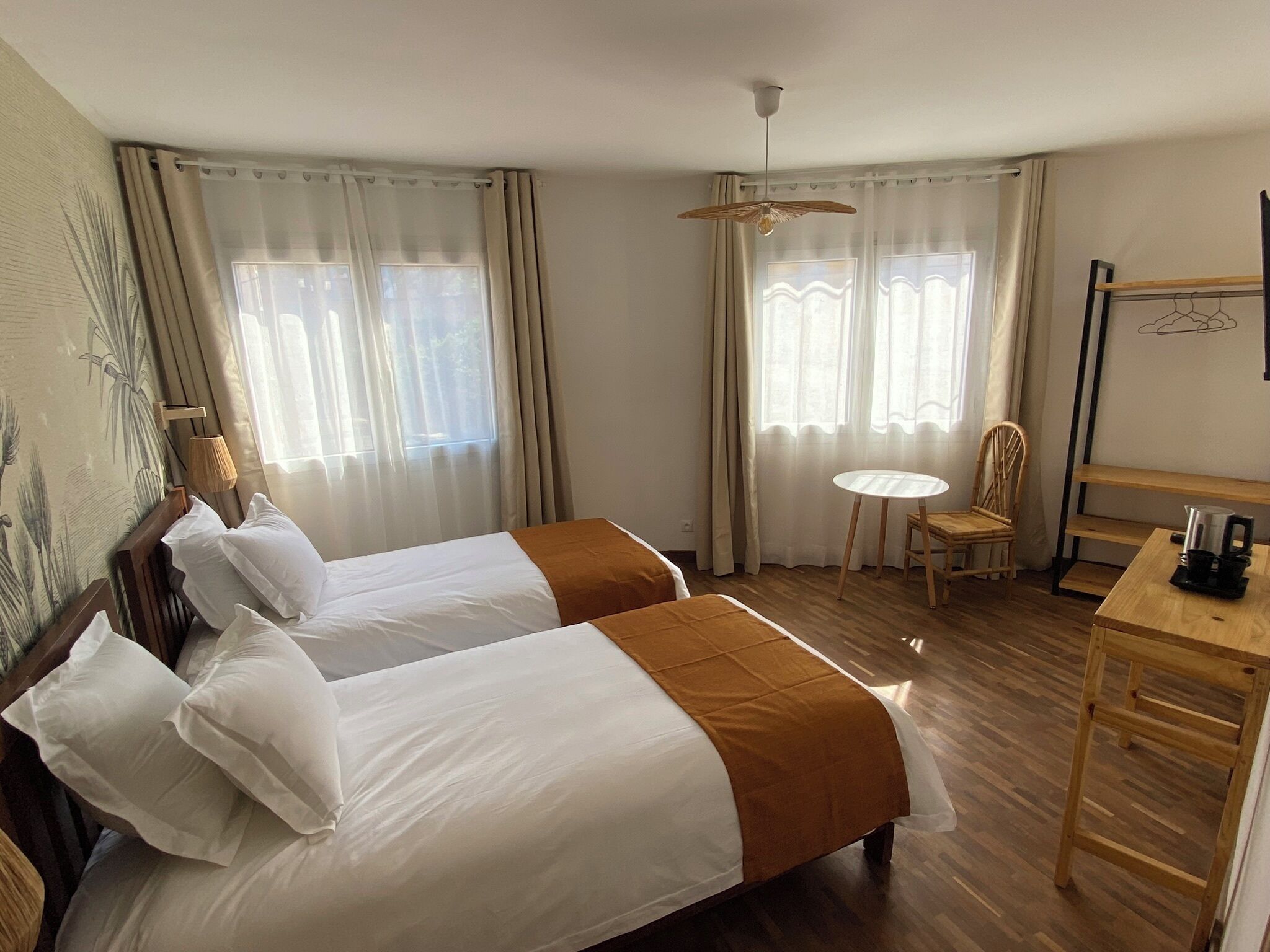 Una camera d'albergo con due letti, un tavolino, una sedia e una ventola a soffitto.