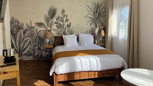 A bedroom with a wooden bed, a small round table, and a wall mural of tropical plants. - Hôtel Escale (Antananarivo)