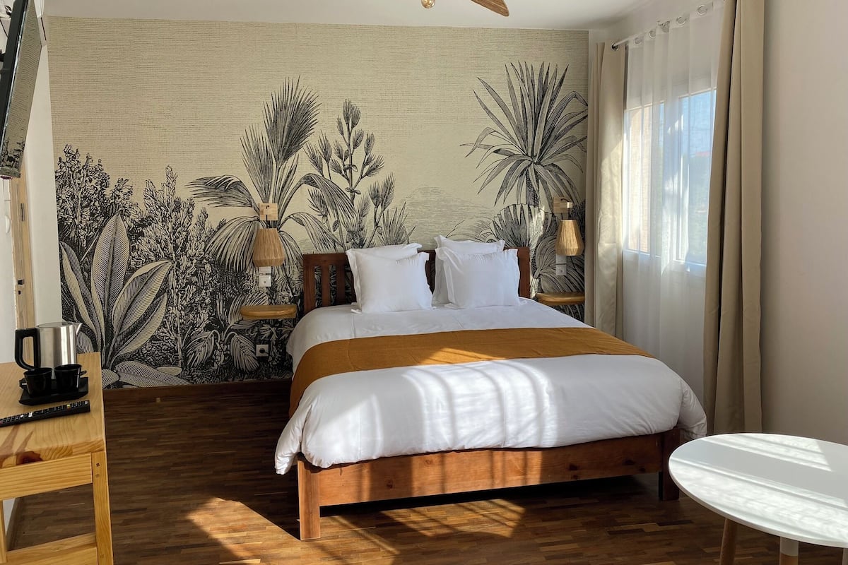 A bedroom with a wooden bed, a small round table, and a wall mural of tropical plants.
