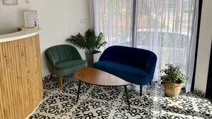 A reception area with a wooden reception desk, a green chair, a blue chair, a small table, and a potted plant. - Hôtel Escale (Antananarivo)