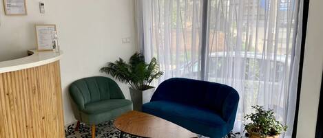 A reception area with a wooden reception desk, a green chair, a blue chair, a small table, and a potted plant.